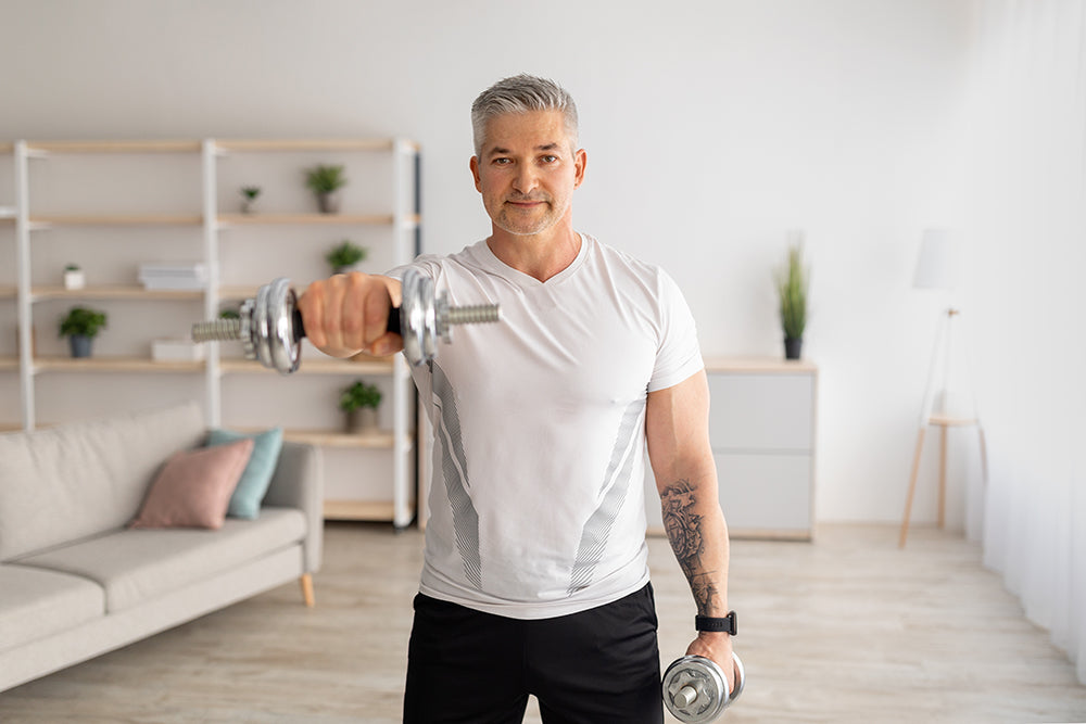 Older man holding a barbell in his right hand in a room