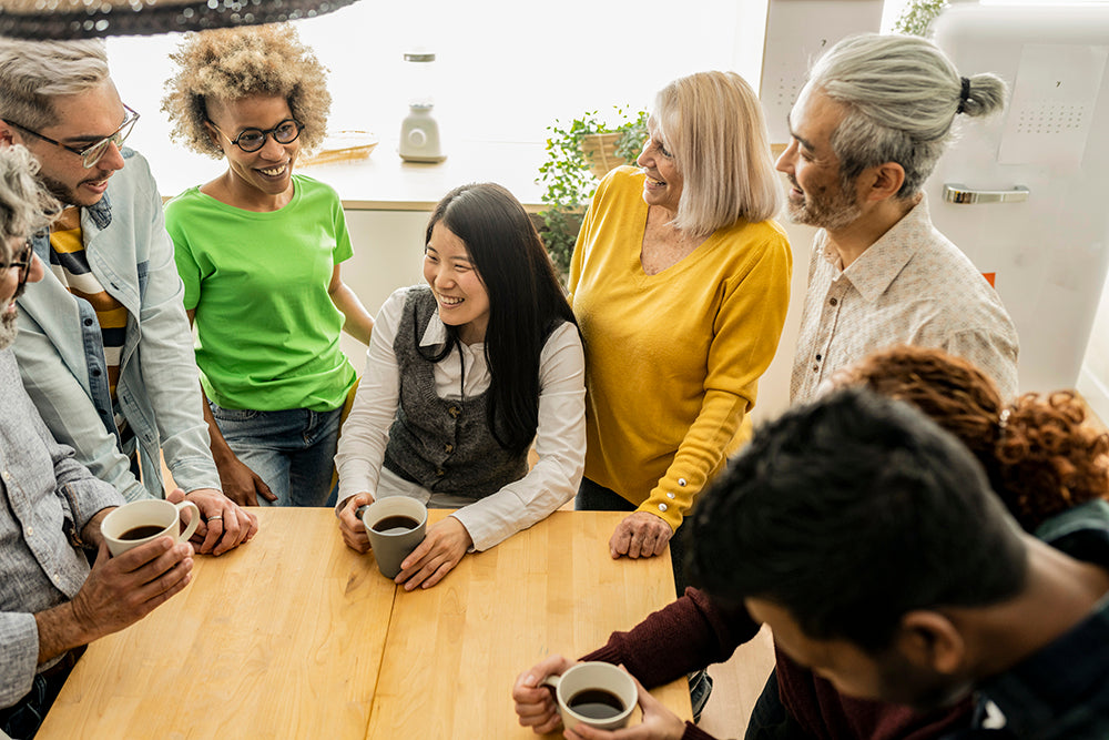 a diverse group of individuals sitting and standing around a table talking